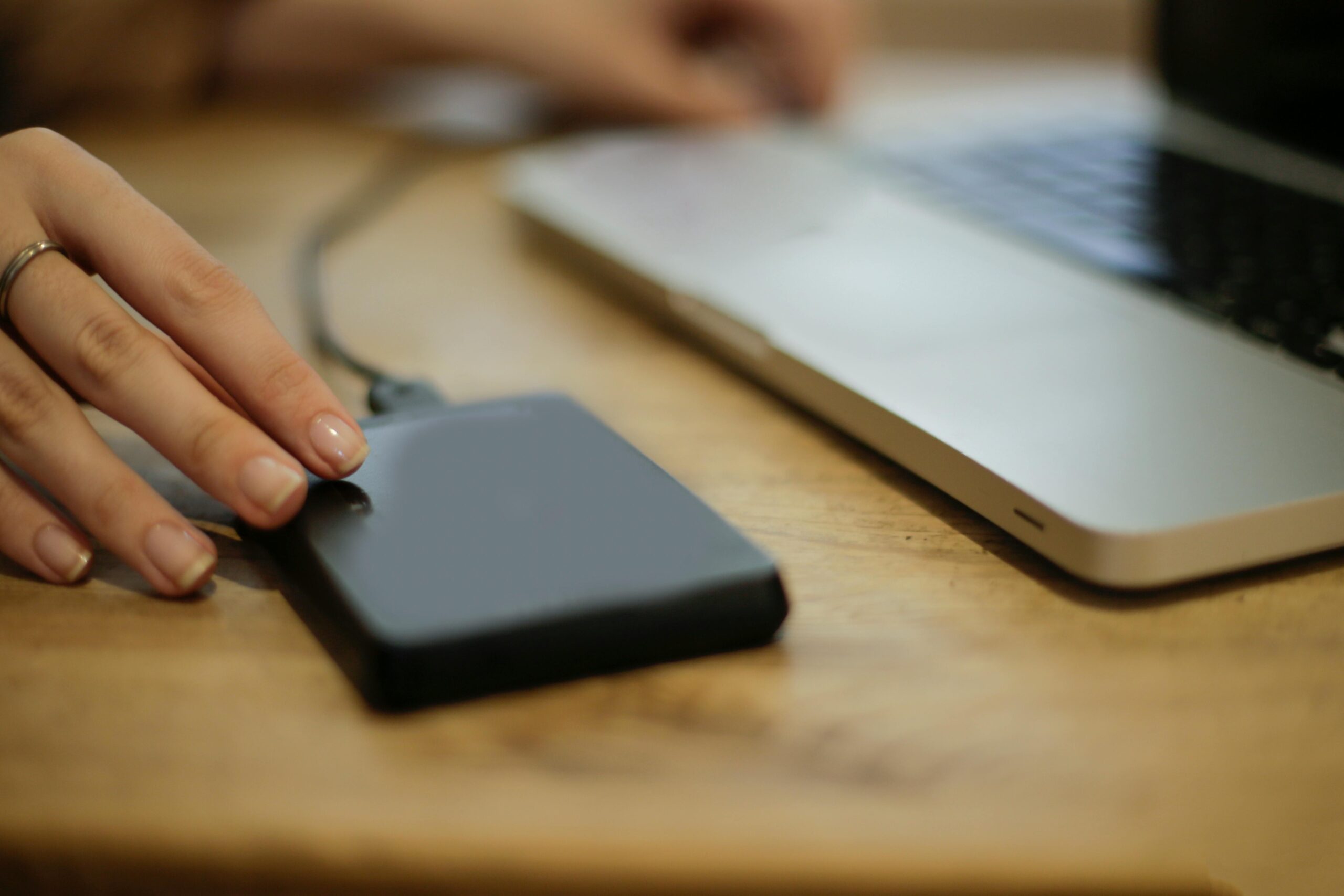 Close-up of a person connecting an external hard drive to a laptop on a desk.